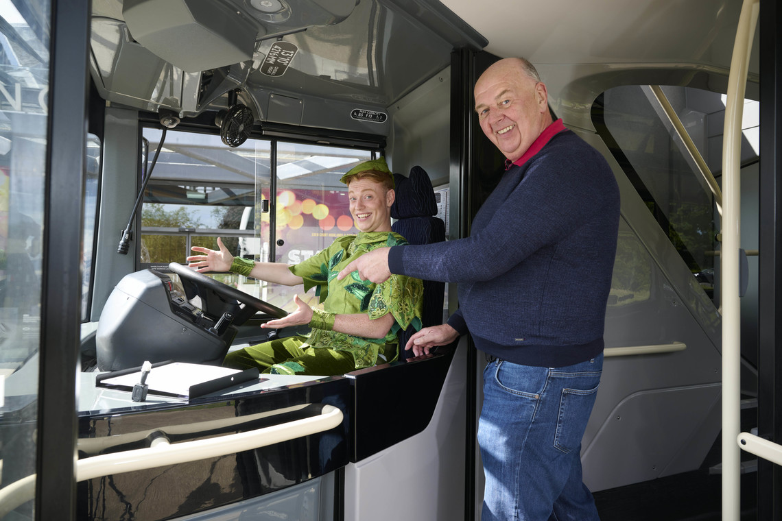 Peter Pan is sat at the driver's seat on a D&E Coach, with Donald from the company stood beside him, pointing to the wheel.